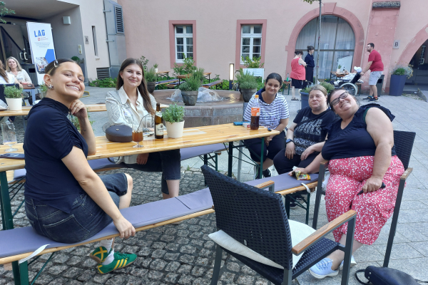 mehrere Frauen sitzen in einem Innenhof um einen Tisch und lächeln in die Kamera