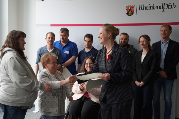 Ministerin Dörte Schall übergibt Katrin Richter und Michaela Seinsoth stellvertretend für die Bewohnenden-Vertretungen den Einberufungsbescheid