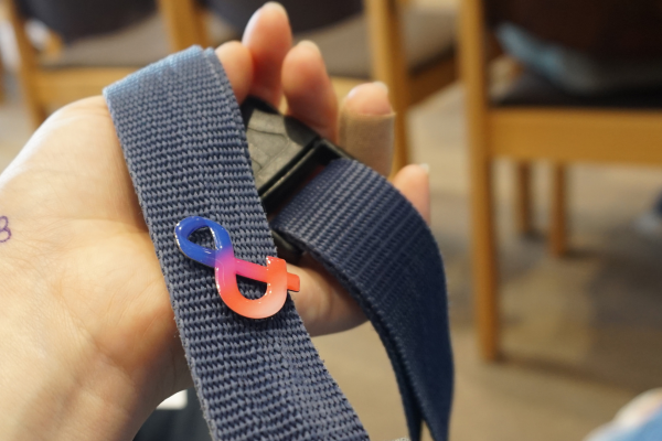 Ein Anstecker in Form eines &-Zeichens in blau und rot auf einem schwarzen Gurt