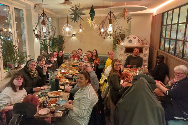 Viele Personen sitzen an Tischen in einem Restaurant und lächeln in die Kamera