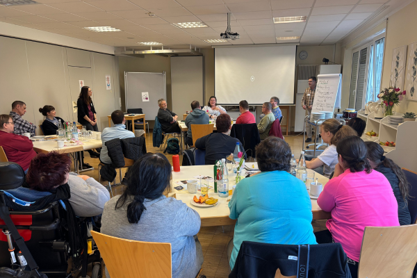 Mehrere Menschen sitzen an Tischgruppen zusammen