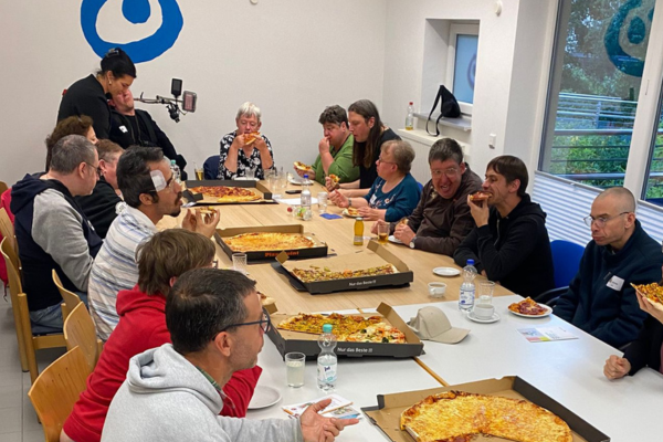 Viele Menschen sitzen an einem Tisch und essen Pizza aus großen Kartons