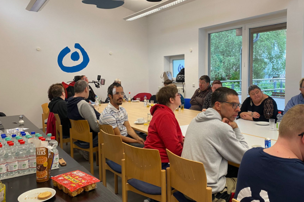Die Aufnahme zeigt eine sitzende Gruppe Menschen um einen Tisch. Im Vordergrund sind Wasserflaschen und Snacks zu sehen. 
