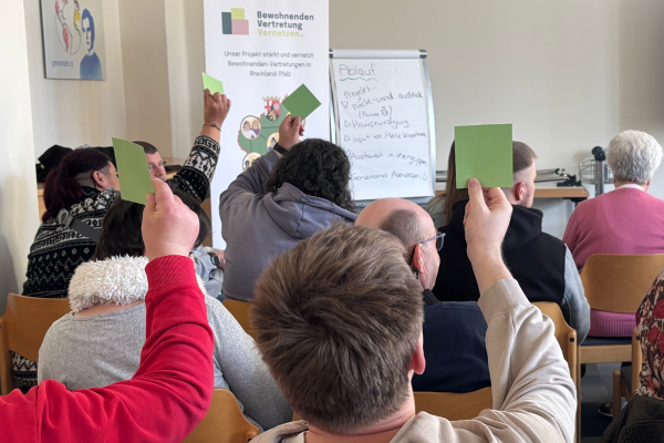 Menschen von hinten, die grüne Kärtchen bei einer Abfrage hochhalten