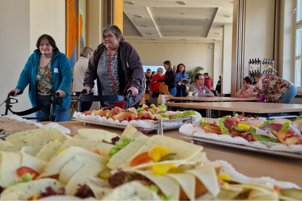 Im Vordergrund belegte Brötchen, im Hintergrund Menschen