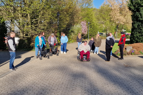 Menschen mit und ohne sichtbare Behinderung stehen draußen im Sonnenschein bei der Geländeführung
