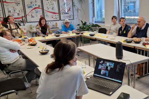 Mehrere Menschen, darunter Herr Speicher, an einem Tisch rund um einen Laptop und ein Konferenzsystem
