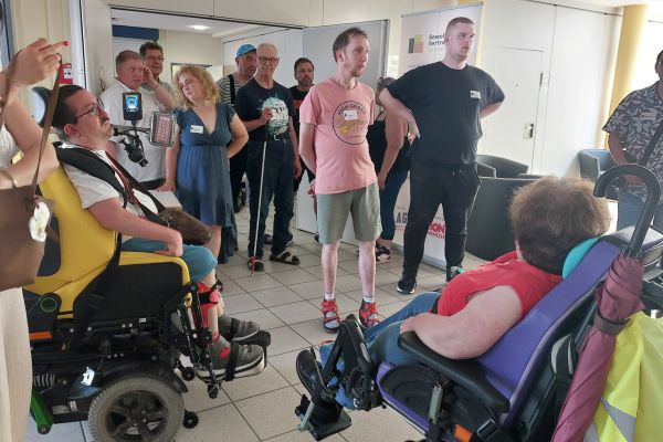 Mehrere Personen im Rollstuhl oder stehend bei einer Hausführung